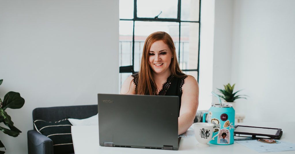 red haired woman working behind a laptop