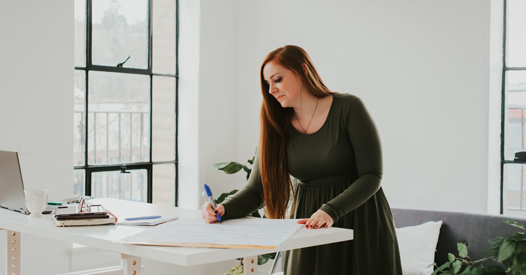 red haired woman standing at table writing